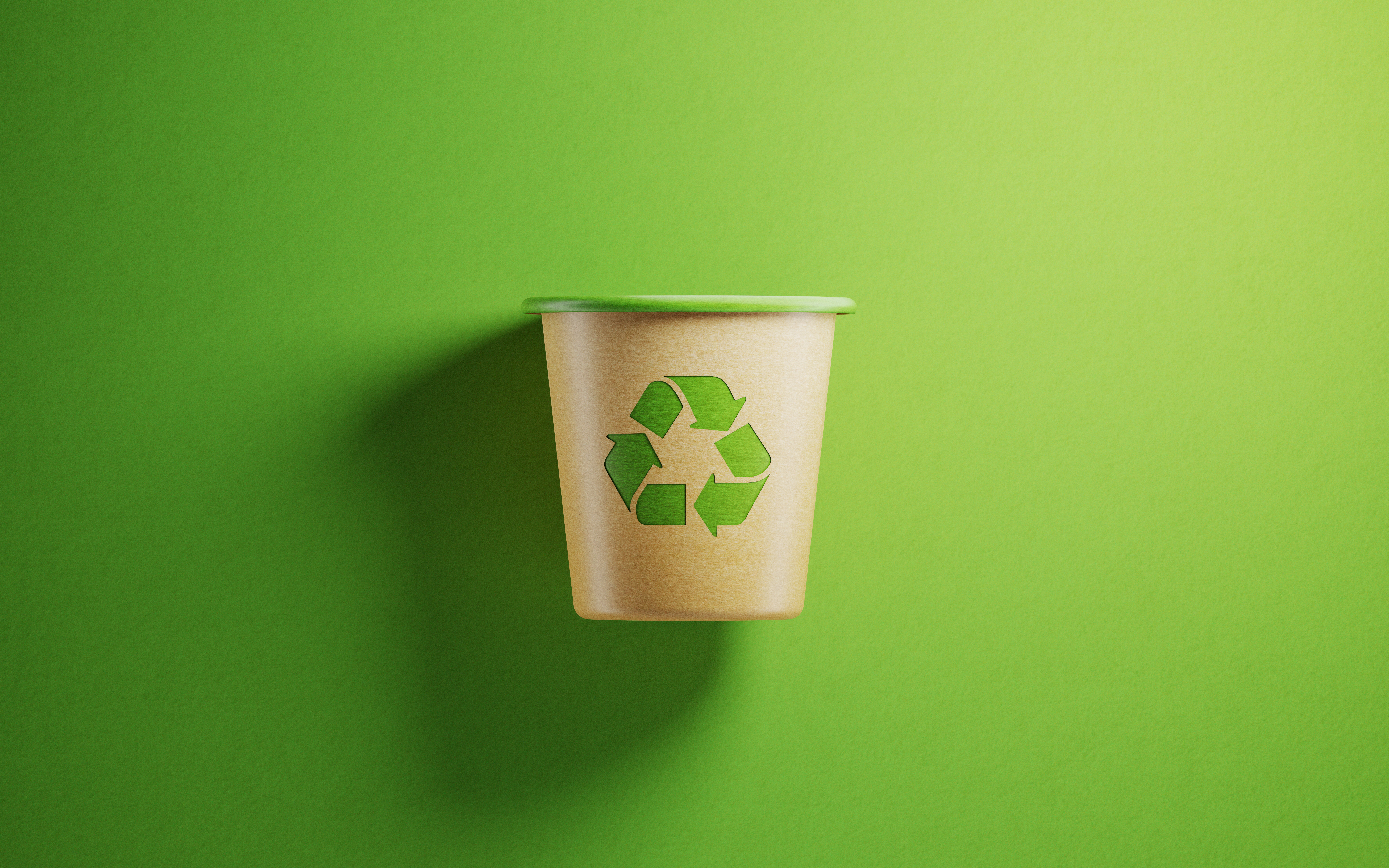 A paper cup with a recycling symbol on top of a green backdrop