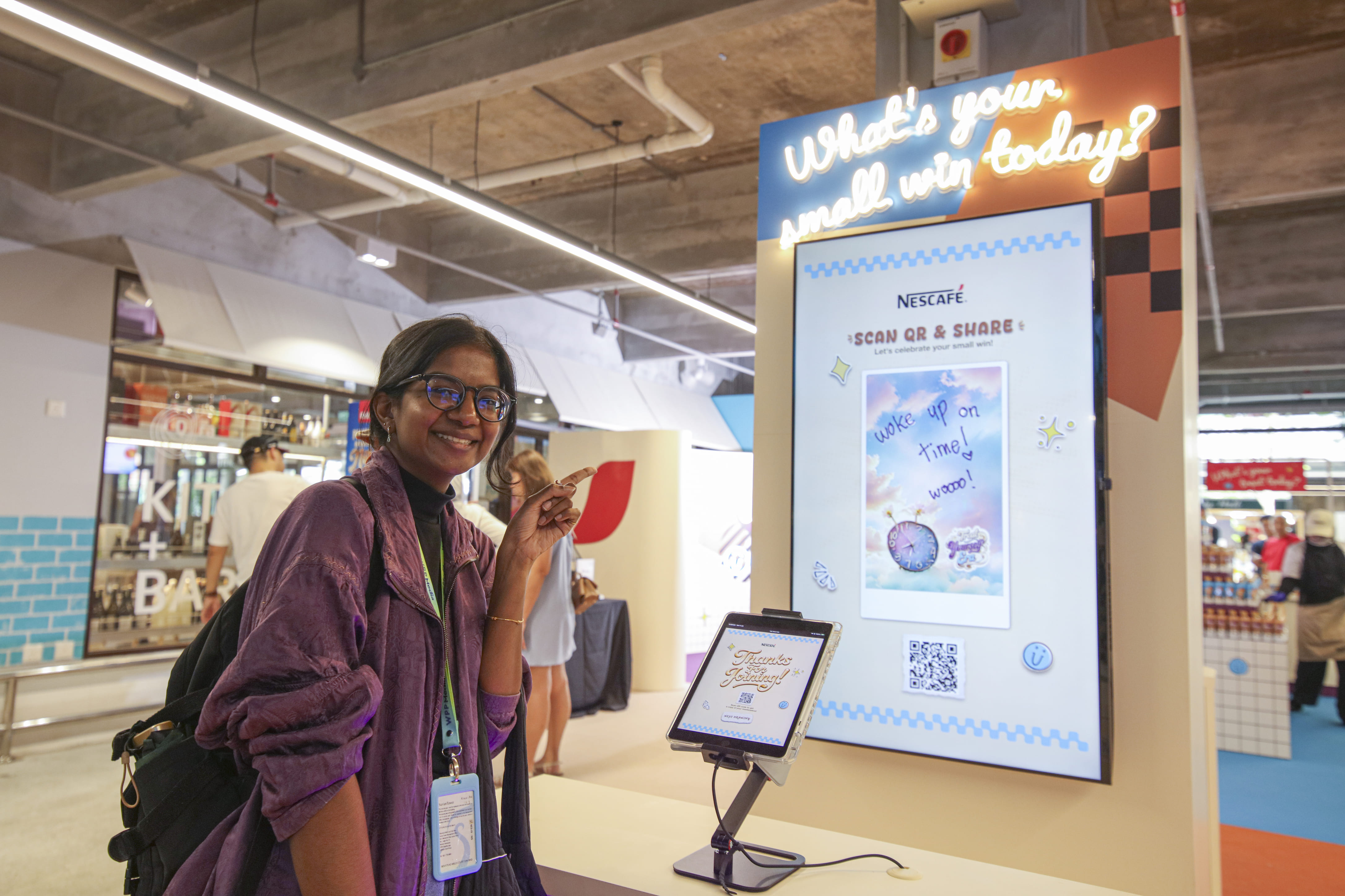 Woman with a ponytail and glasses smiling while pointing at qr code